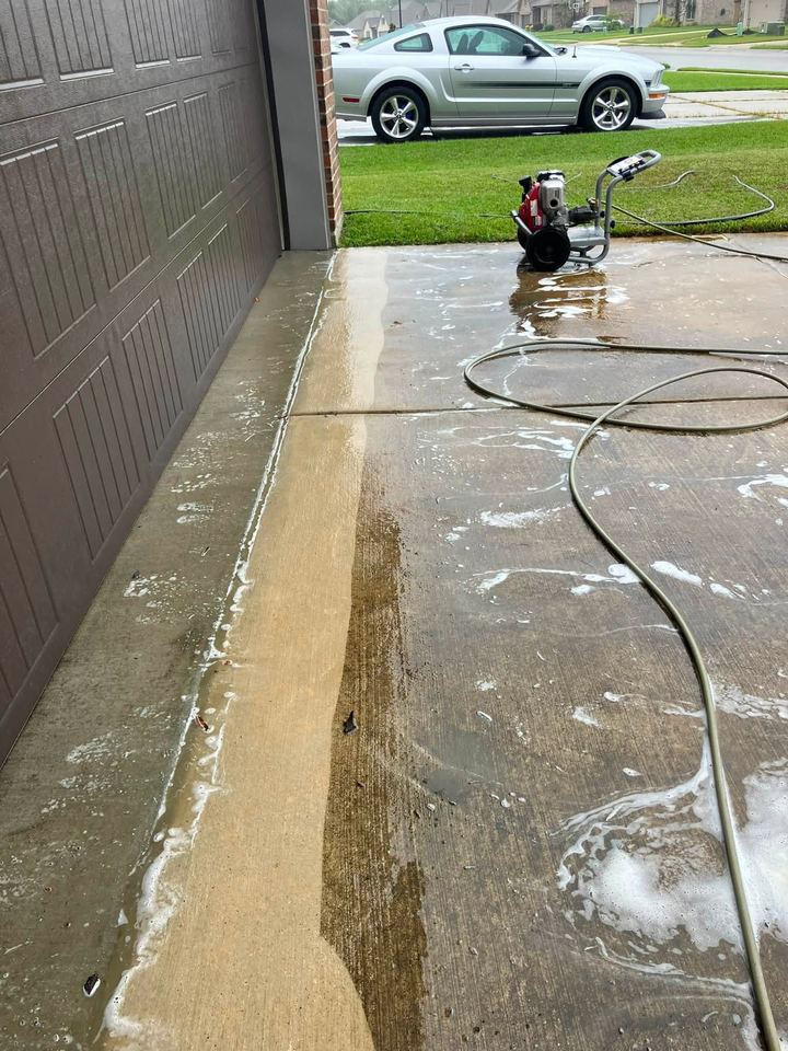 The same driveway part-way through the wash, with a clean stripe beside the pressure washer and hoses.
