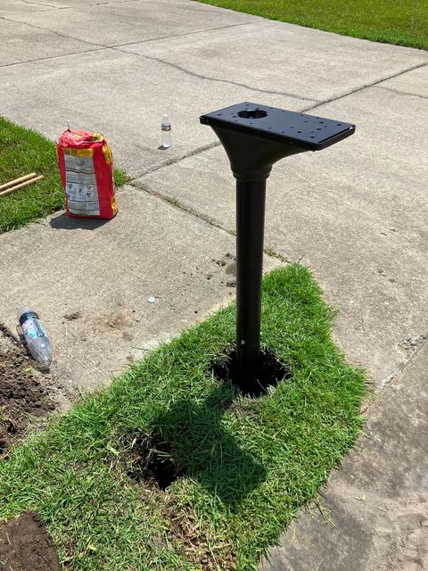 A new black mailbox post set into the ground at the edge of a driveway.
